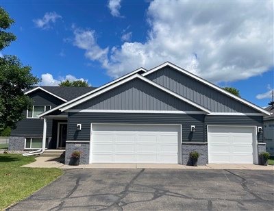 A modern two-story house with a gray exterior, double garage, and well-kept lawn under a clear sky.