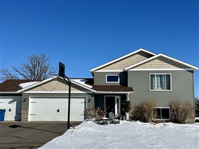 A split-level house with a beige exterior and white garage, surrounded by snow under a clear blue sky.