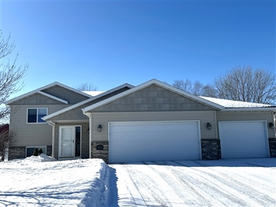 A sprawling single-story house with beige siding and a triple car garage, set against a snowy landscape and clear blue sky.