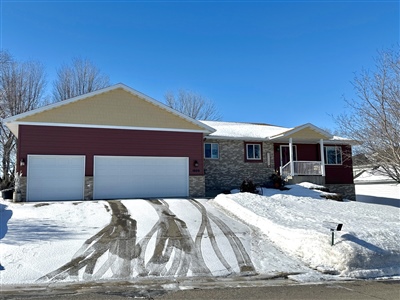 A single-story house with red doors and stone facade, featuring a double garage and a snow-covered driveway under a clear blue sky.