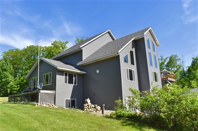 A modern, angular gray house with multiple stories and asymmetrical design, nestled in a lush green setting under a clear sky.
