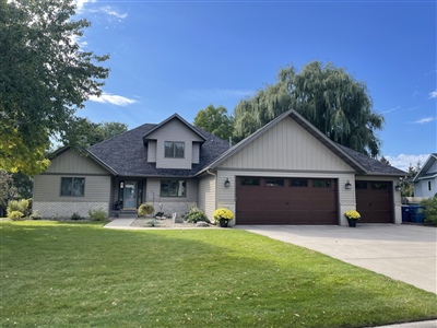 A contemporary house with a sloped roof and double garage, surrounded by a well-maintained lawn under a sunny sky.