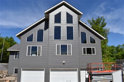A tall three-story home with a gray facade and multiple garage doors, located under a bright blue sky.