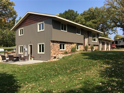 A contemporary split-level home with a gray and stone facade, featuring a spacious patio area, set in a grassy yard.