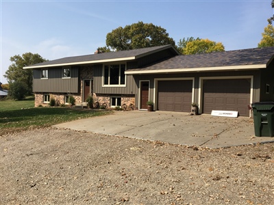 A split-level house with a gray and stone exterior, double garage, and a gravel driveway, set in a residential area.