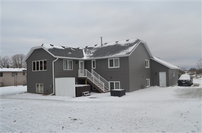 A large gray duplex with multiple entrances and stairs, covered in fresh snow under a cloudy winter sky.