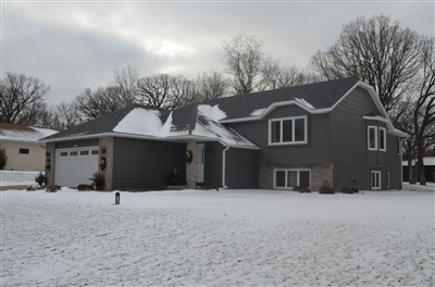 A spacious gray home with multiple gabled roofs and a large garage, set in a snowy landscape with bare trees.