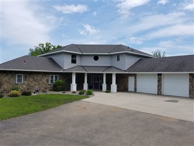 A luxurious house with a stone and gray facade, featuring a prominent circular window, columns, and a triple garage.