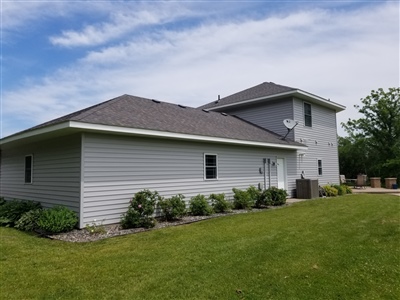 A modern home with a gray exterior, featuring a large side lawn and small decorative plants under a clear sky.