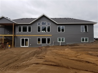 A large, gray two-story building under construction, with multiple windows and doors, situated in a muddy construction site.