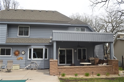 A blue two-story house with a covered patio and brick accents, featuring a pool area and bare trees in the background.