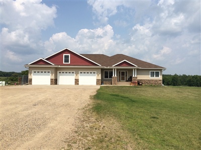 A single-story house with beige siding and a red roof, featuring a double garage and a gravel driveway, set against a cloudy sky.
