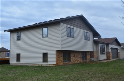 A modern two-story home with light gray siding and brick accents, featuring a side entrance and an overcast sky backdrop.