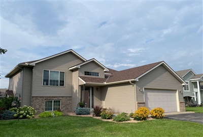 A modern beige split-level house with a double garage and well-kept lawn, located in a suburban neighborhood under a cloudy sky.