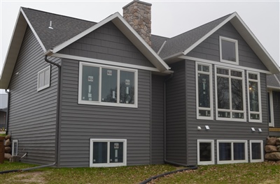 A contemporary home with dark gray siding and multiple angular roof lines, featuring large windows and a stone chimney.