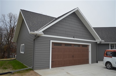 A section of a modern gray house showing a large garage with a brown door and distinctive angular roof design.