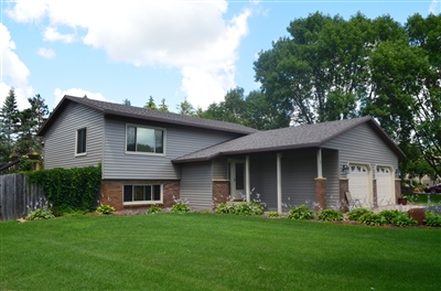 A charming split-level house with gray siding and brick accents, featuring a well-landscaped lawn with mature trees.