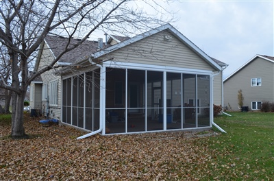 A beige house with a screened-in porch on the side, surrounded by a yard with fallen leaves and bare trees.
