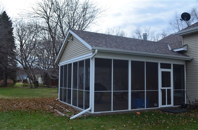 A beige house with a screened-in porch on the side, surrounded by a yard with fallen leaves and bare trees.