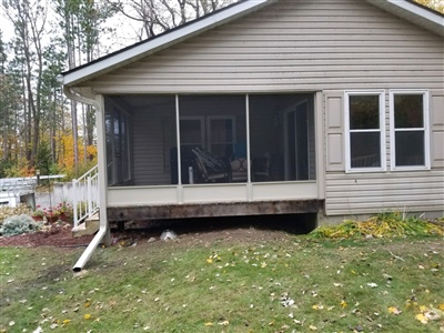 A beige house with a screened-in porch on the back, overlooking a grassy yard with fallen leaves and trees in the background.