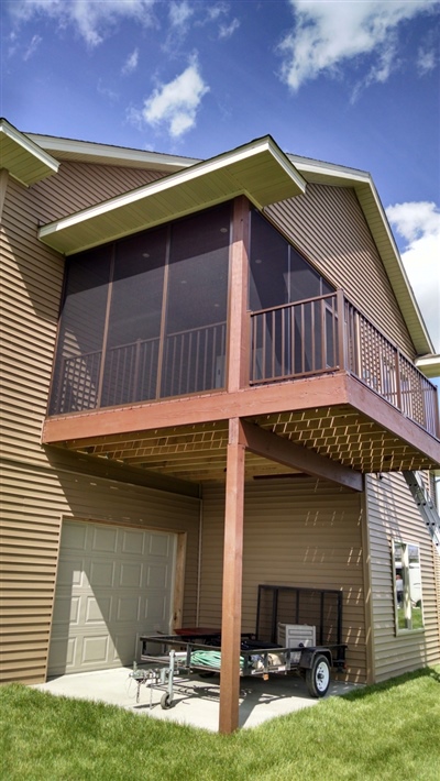 A two-story house with a raised screened-in porch supported by wooden beams, and an open area underneath used for storage.