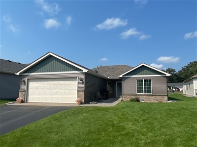 A modern single-story house with beige siding, featuring a double garage and a neatly manicured lawn under a clear blue sky.