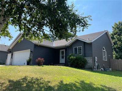 A modern house with dark gray siding, featuring a single garage and lush green lawn partially shaded by a large tree.