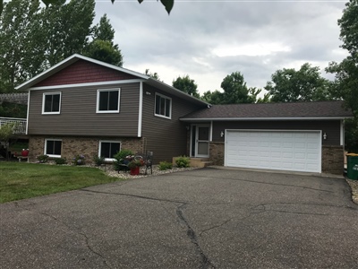 A split-level home with gray and stone accents, featuring a double garage and a driveway, set in a residential area with greenery.