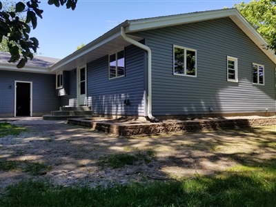 Single-story gray house with a large front yard and multiple entrances under clear skies.