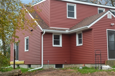 Red two-story home with white trim and surrounding greenery on an overcast day.