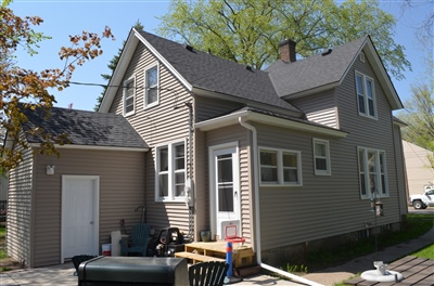 Two-story taupe house with attached garage and driveway on a sunny day with clear skies.