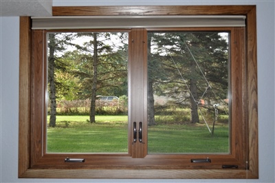  A view through a large wooden-framed window overlooking a lush green lawn and mature trees, providing a serene indoor perspective.
