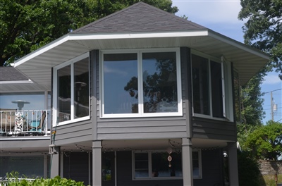 A two-story gray house with a large octagonal bay window on the upper floor and a patio area below.