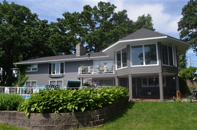 A two-story gray house with a large octagonal bay window, multiple balconies, and a landscaped garden in the front yard.