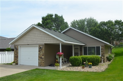 A neat single-story house with beige siding, featuring a single car garage and beautifully landscaped front yard.